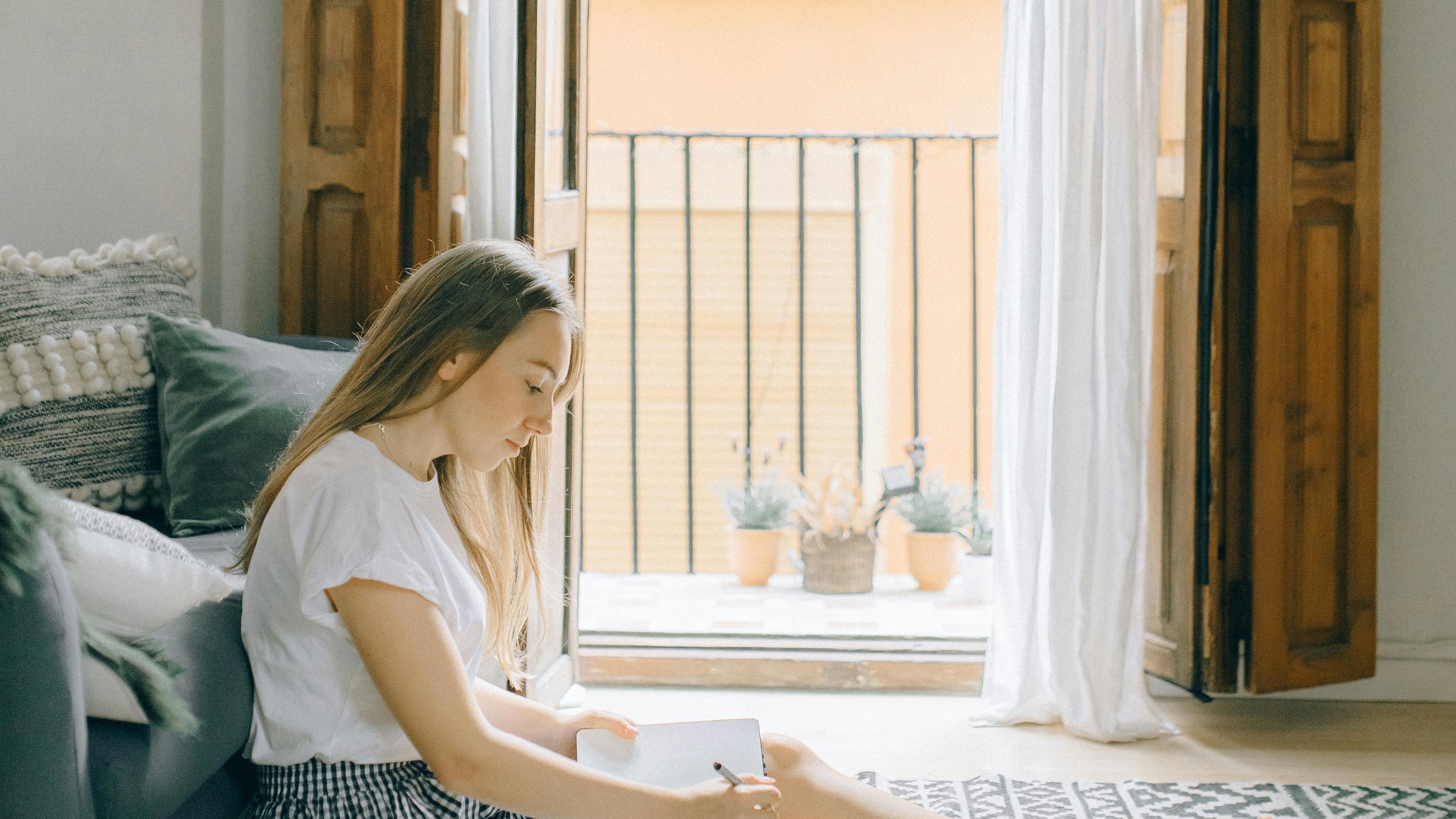 Woman sitting on a rug in a room with large windows and a view of a balcony.